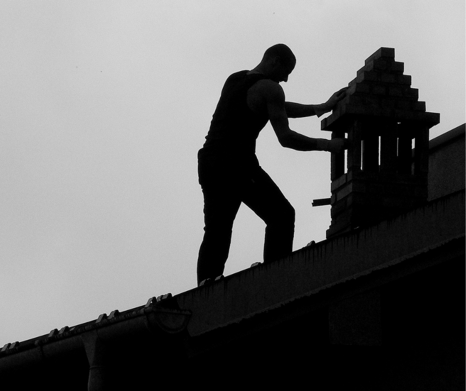 Chimney sweep on roof building chimney, the image is quite dark and more of a silhouette.