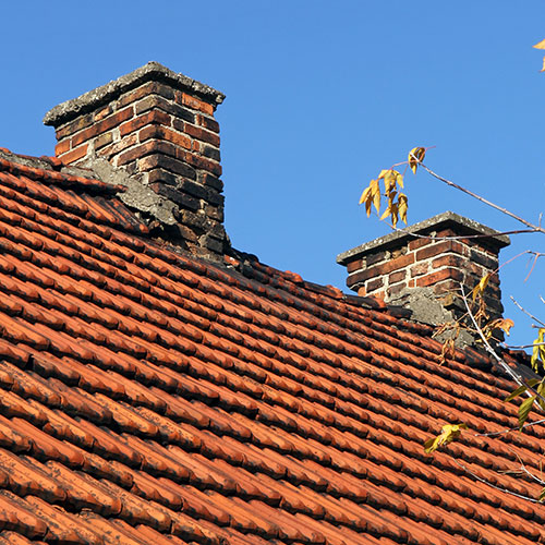 Chimneys deteriorating on older home with terra cotta shingles.  There is a blue sky in the background and a bare limb on the right.