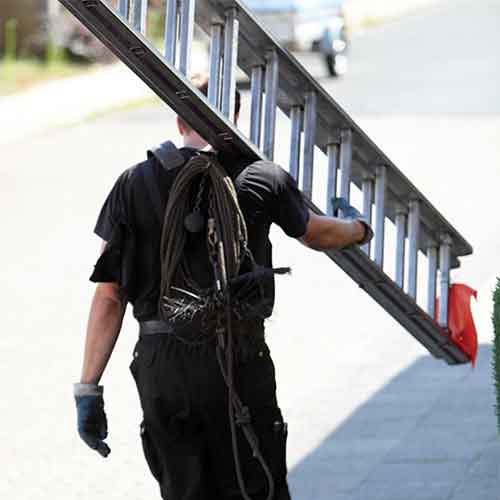 Chimney Sweeping - Sweep carrying a ladder with an orange flag on it.  He is wearing gloves.