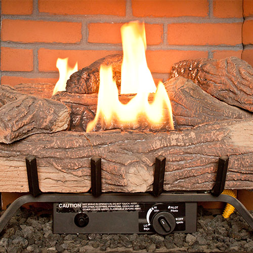 Gas Log Fireplace with fire, red firebrick in the box, logs sitting on a grate with the gas control at the bottom and ash layered below the grate.