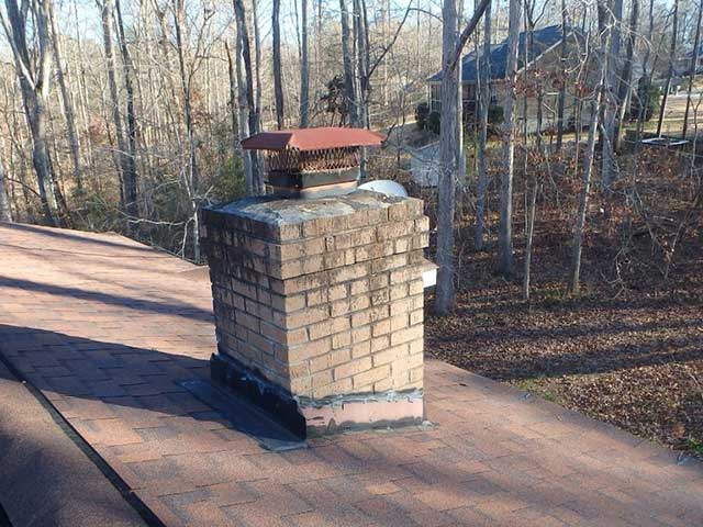 Before - Chimney with rusted cap and cage with bare trees and a home in the background.
