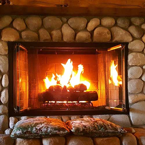 Gas Fireplace with large river rock surround and hearth.  It has a screen.  There are two pillows sitting on the hearth. It is beautiful!